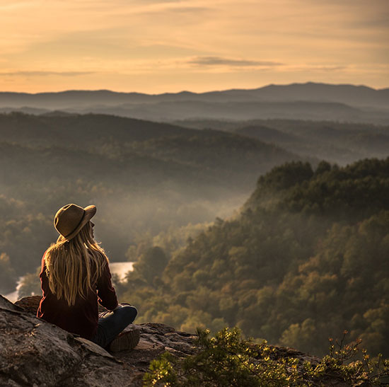 femme de dos au chapeau assise au sommet d'une montagne